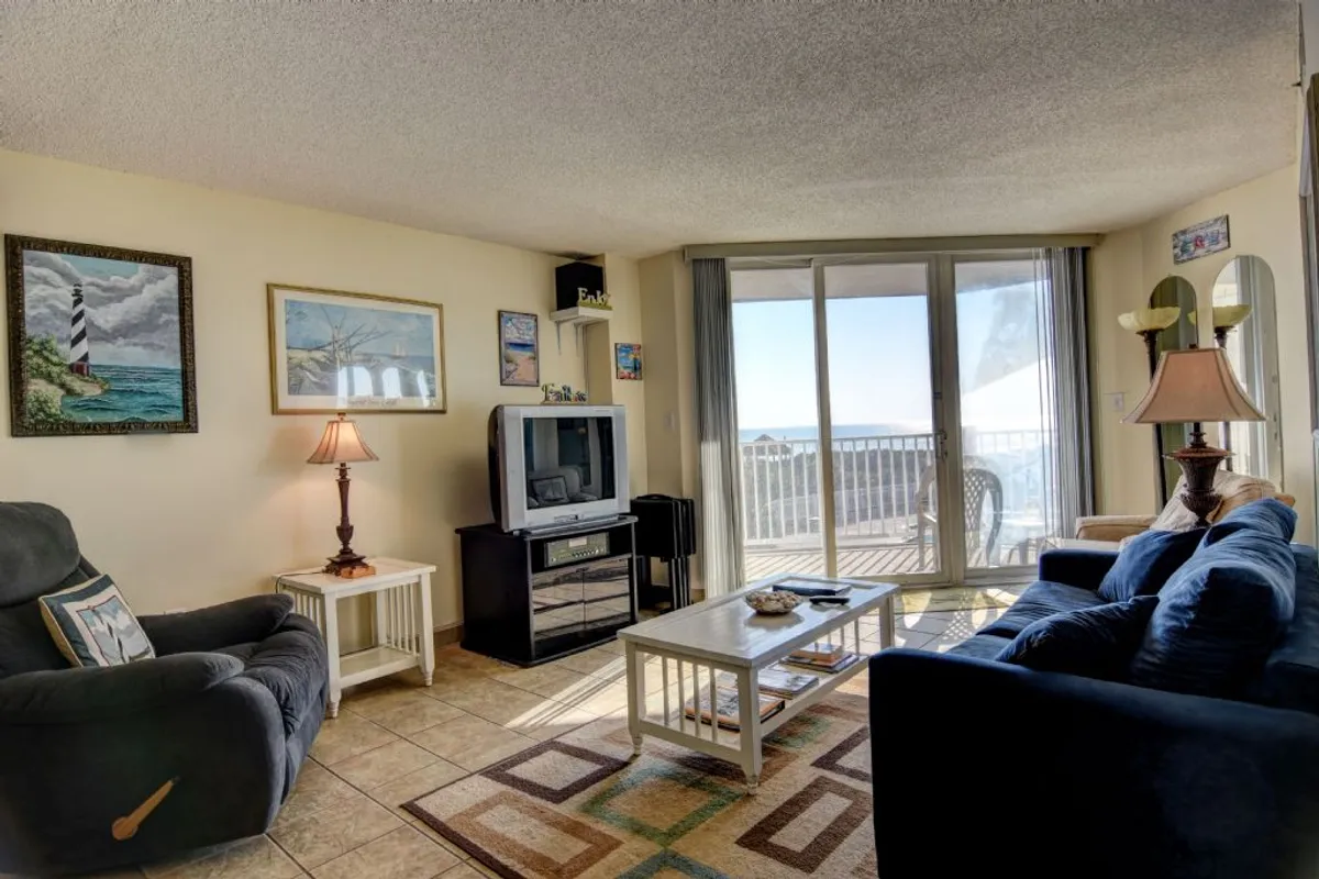 A comfortable living space with a modern sofa, coffee table, television, and a sliding glass door that opens to stunning ocean views. The open layout allows natural light to flow throughout, creating a welcoming environment for relaxation and socializing.