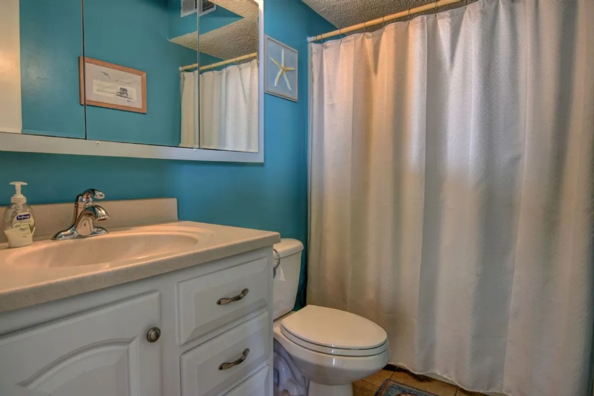 A fresh and inviting bathroom with blue walls, white cabinetry, a large mirror, and modern fixtures. The space is bright and tranquil, designed for relaxation and self-care.