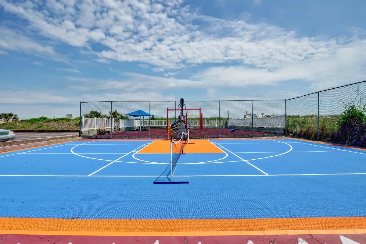 This exterior image showcases a vibrant basketball court with colorful flooring and a net, set against the backdrop of a sunny day. The court is designed for both basketball and tennis, and nearby, you can imagine community members or families gathering for friendly games.