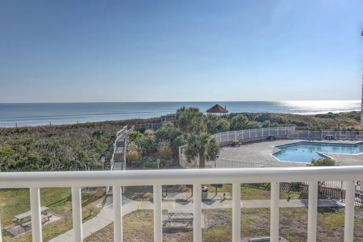 The image showcases a sparkling, covered saltwater pool set amidst beautifully landscaped grounds, with a charming gazebo nearby. Beyond the pool, there are sweeping, unobstructed views of the Atlantic Ocean and a sandy shoreline—perfect for watching the sunrise. The scene evokes a tranquil, resort-like atmosphere, inviting guests to relax, swim, bask in the sun, or gather for a poolside picnic.