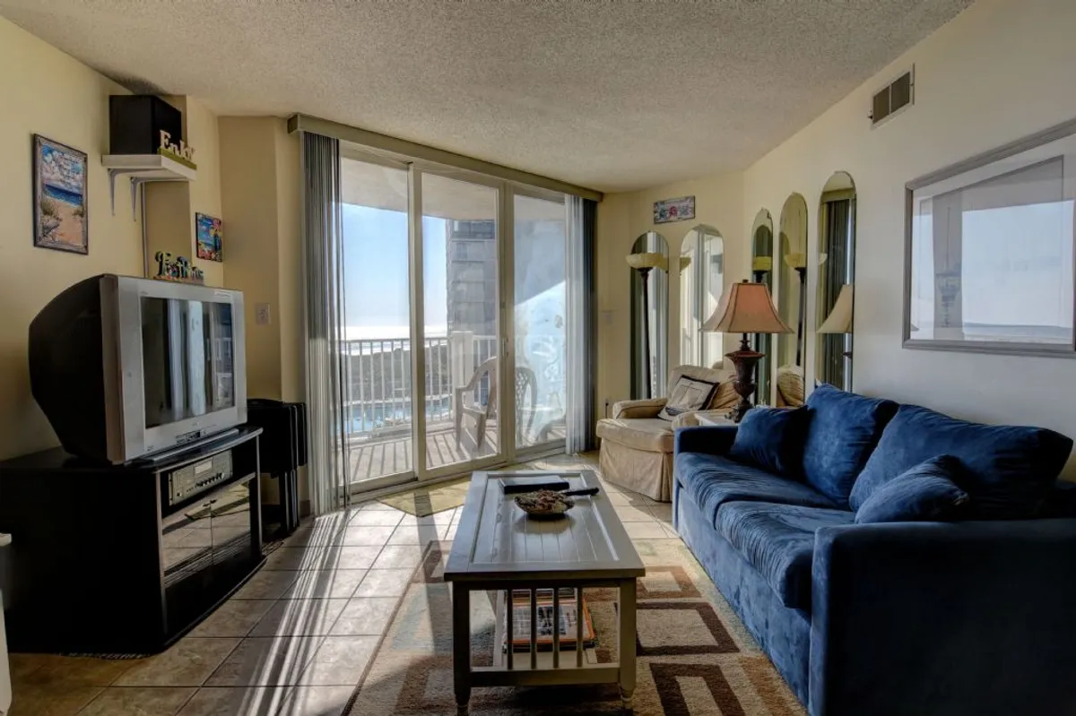 A bright, inviting living room featuring a plush sofa and coffee table, with a television and large sliding glass doors that reveal expansive ocean views. Natural light bathes the space, making it perfect for socializing, relaxing, or enjoying the scenery.
