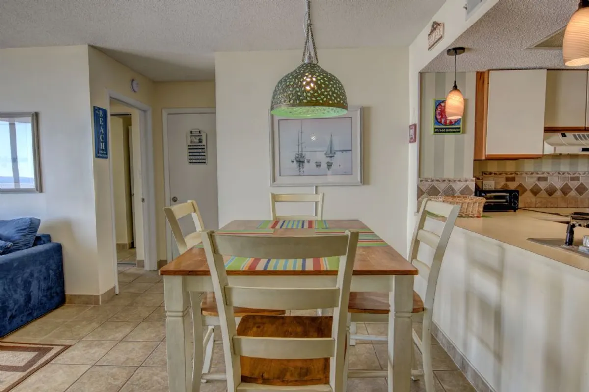 A cheerful dining area featuring a dining table with a colorful runner, illuminated by a distinctive green pendant light. The space is set up for family meals, casual gatherings, and board games, embodying the spirit of shared experiences.